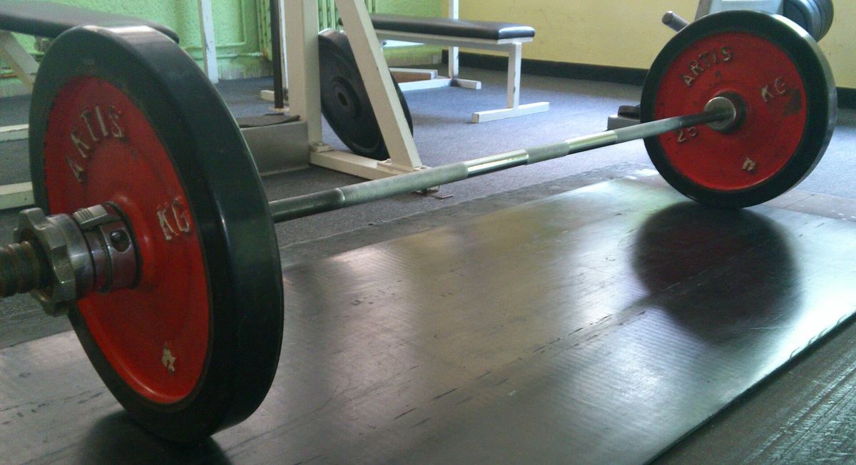 Langhantel mit Gewichtsscheiben liegt auf dem Boden eines Trainingsraums