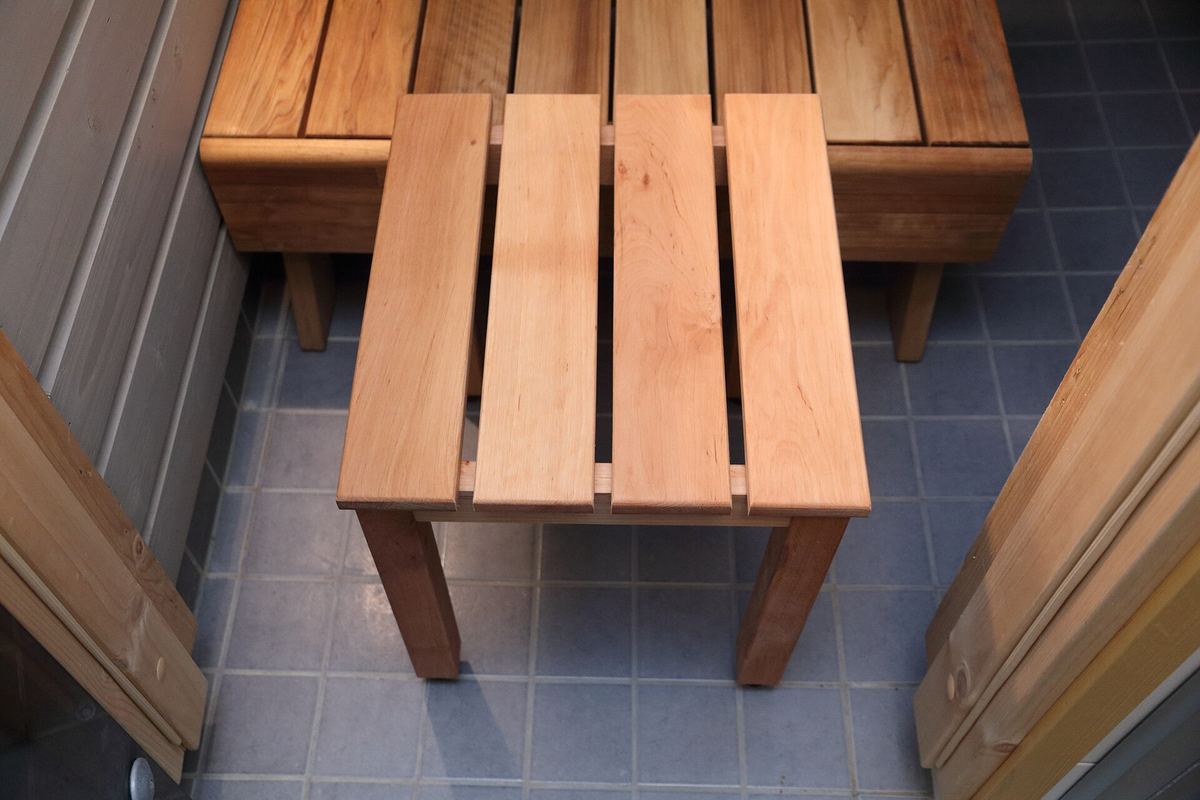 Holzbänke und ein Saunahocker in einer hellen Saunakabine